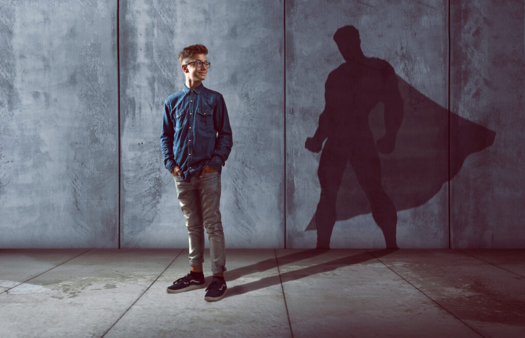 Image of a young male looking back at his shadow that is of a super hero.