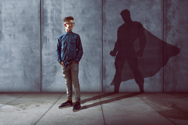 Image of a young male looking back at his shadow that is of a super hero.