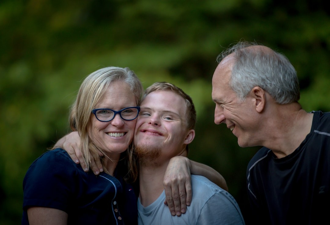 Young man with Down's syndrome smiling and hugging his two middle aged parents